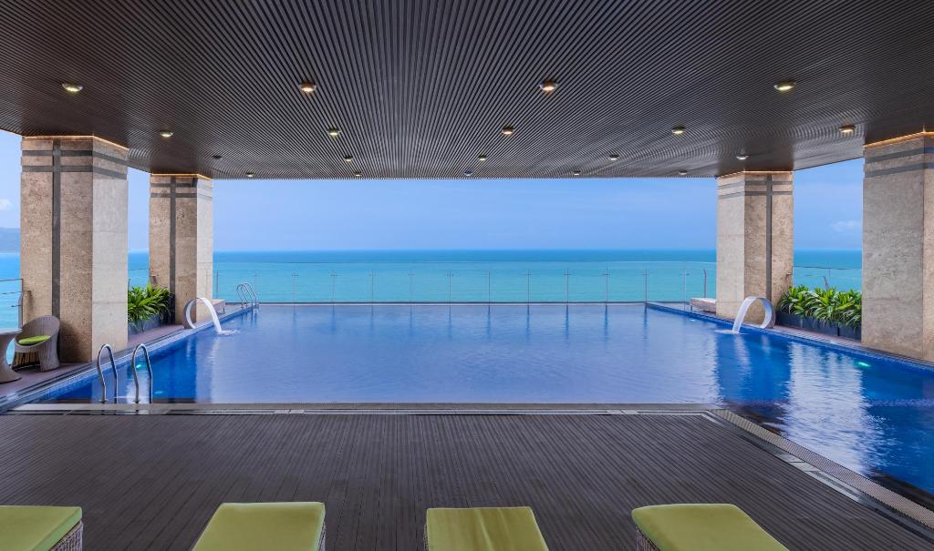 Outdoor swimming pool at Rosamia Da Nang Hotel, with white loungers, umbrellas and the hotel tower behind the palms