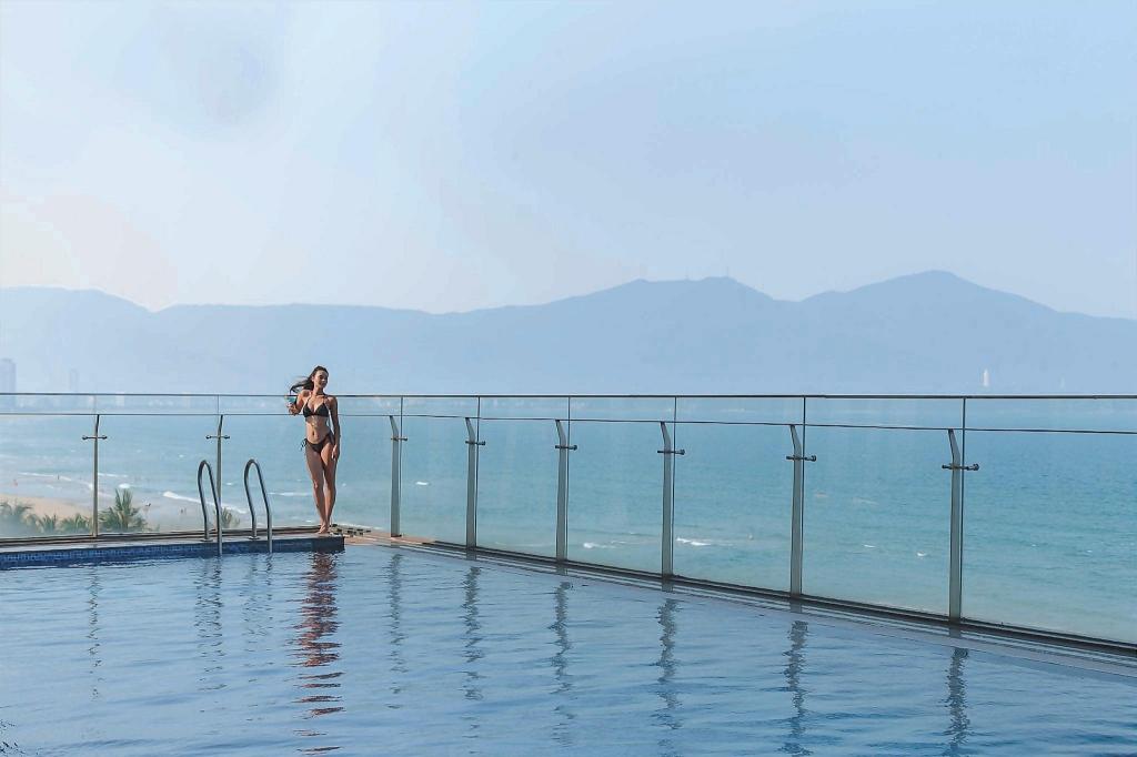 Infinity-edge swimming pool at Rosamia Da Nang Hotel, with lounge chairs, palms and the hotel tower behind