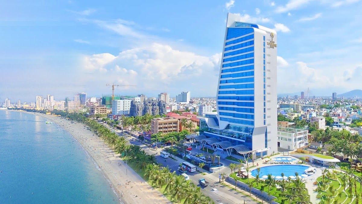 Aerial view of My Khe Beach in Da Nang showing a large beachfront hotel tower, pool complex, palm-lined shore and the city skyline