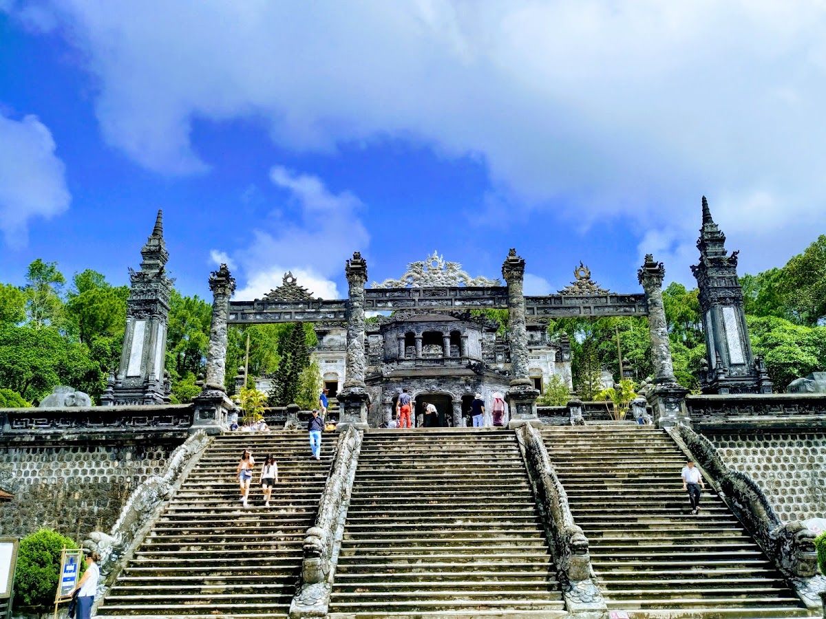 Khai Dinh Tomb entrance stairway with stone columns and the main gate-pavilion at the top, visitors climbing the wide steps